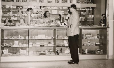 Two women stand behind the counter at the gift shop while a man shops.