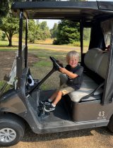 Callan, a young boy, driving a golf cart at the golf tournament