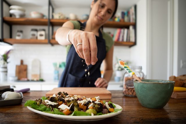 Close-up of a woman's hand sprinkling seasoning over a salad