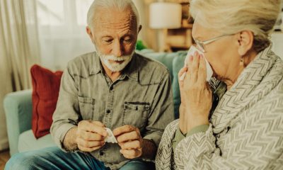 man opens medication packet near woman using tissue on nose