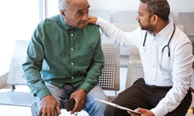 Bearded doctor sits and talks with older man in green button-up shirt