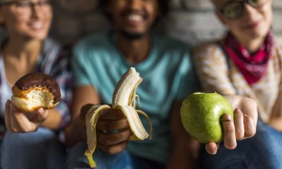 Three people holding something different, a donut, a banana and an apple