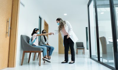 Female doctor greeting young patient and her mom in the hallway of a hospital.