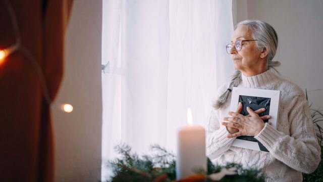 Woman with long silver hair holds a book to her chest and looks out the window