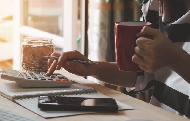 Closeup of a person's fingers using calculator and holding a coffee cup