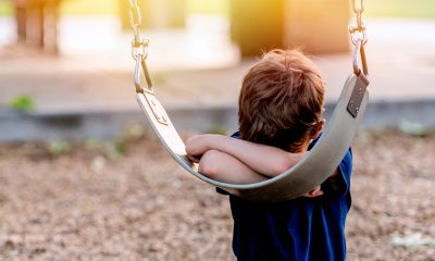 young boy with head in his arms against a playground swing
