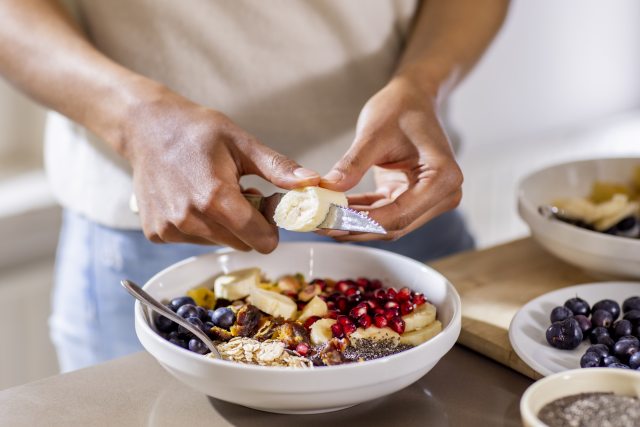 Woman cutting banana to add to a fruit bowl.