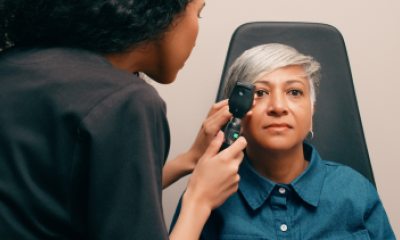 A woman with short gray hair gets her eyes examined by an optometrist.