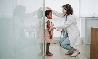 Young girl stands next to wall as doctor measures height