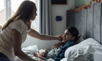 A long-haired adult woman cares for a young person in bed