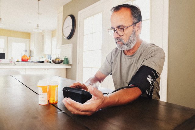 Man with beard measures blood pressure at kitchen table