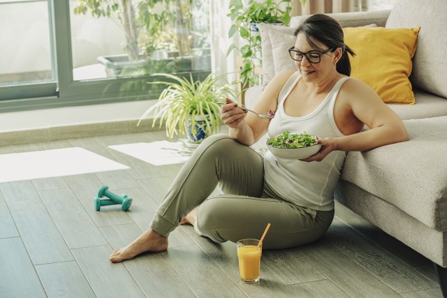 Person sits on floor next to couch, eating a salad