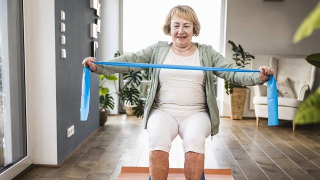 Woman sits in chair, stretching a resistance band
