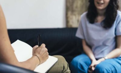 A person takes notes while another in the background speaks
