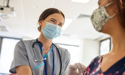 A masked nurse smiles and provides care to a patient