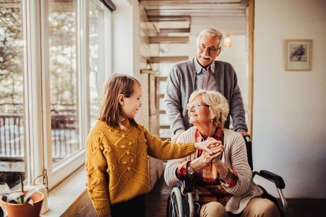Young girl visits grandmother in wheelchair, grandfather behind