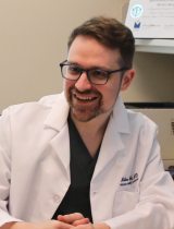Dr. Matthew Gust smiling in his office with a diploma in the background