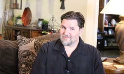 A man in a brown shirt sitting on a living room couch