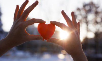 Close-up of hands holding a heart shaped item up to the sunlight