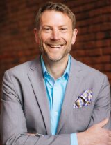 Photo of Matt Sayre in a gray suit with a bright blue shirt 
