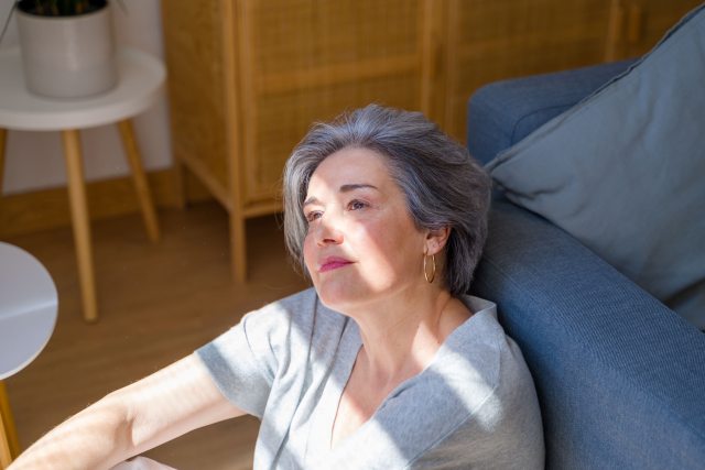Woman with short silver hair looks up from floor into filtered sunlight 
