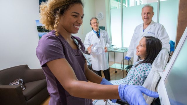 A smiling nurse in the foreground provides care to a patient