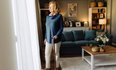 Smiling woman stands near sunny door with help of a cane