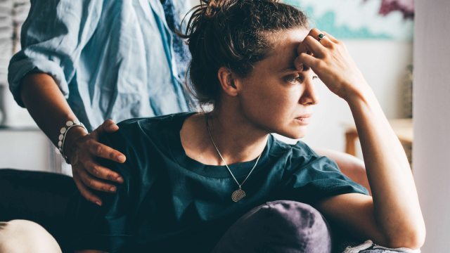 Standing woman puts comforting hand on shoulder of worried woman